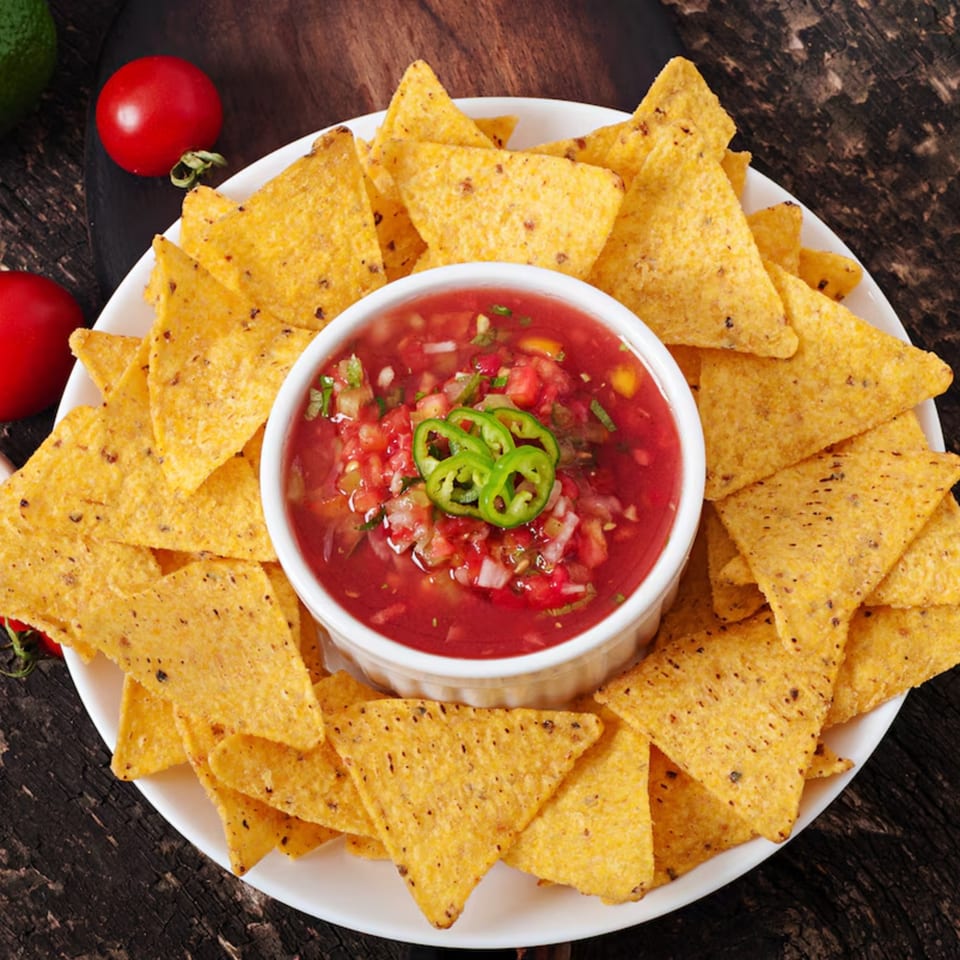 A white plate filled with crispy tortilla chips surrounds a bowl of fresh salsa, garnished with jalapeños.