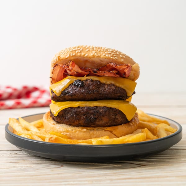 Double cheeseburger with bacon and a side of golden french fries on a dark plate.