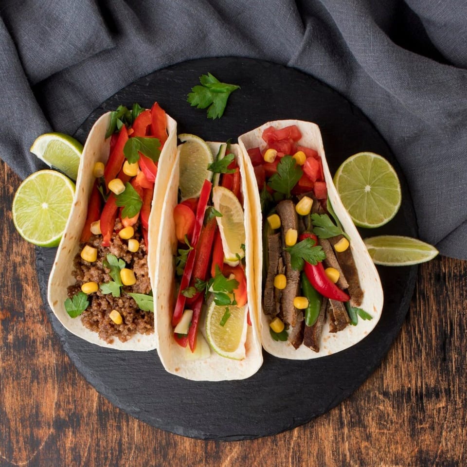 Three Sundaes Fast Food tacos, one with ground beef, one with chicken, and one with steak, on a black platter.